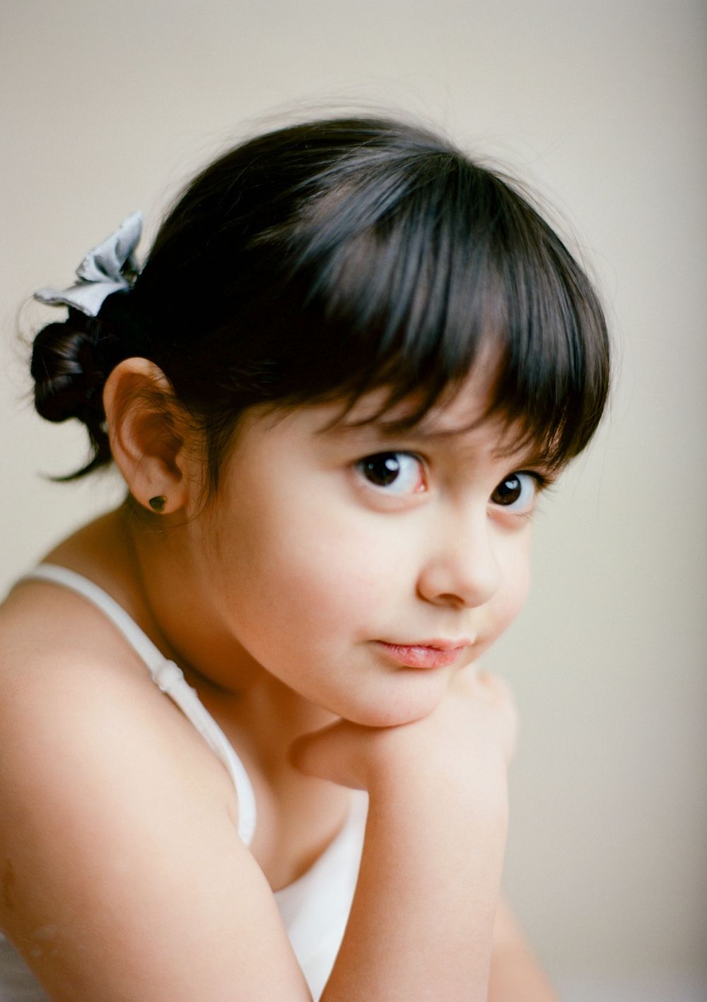 Dark haired 4 year old girl with hair tied in two buns tied with blue ribbon in a neutral studio setting