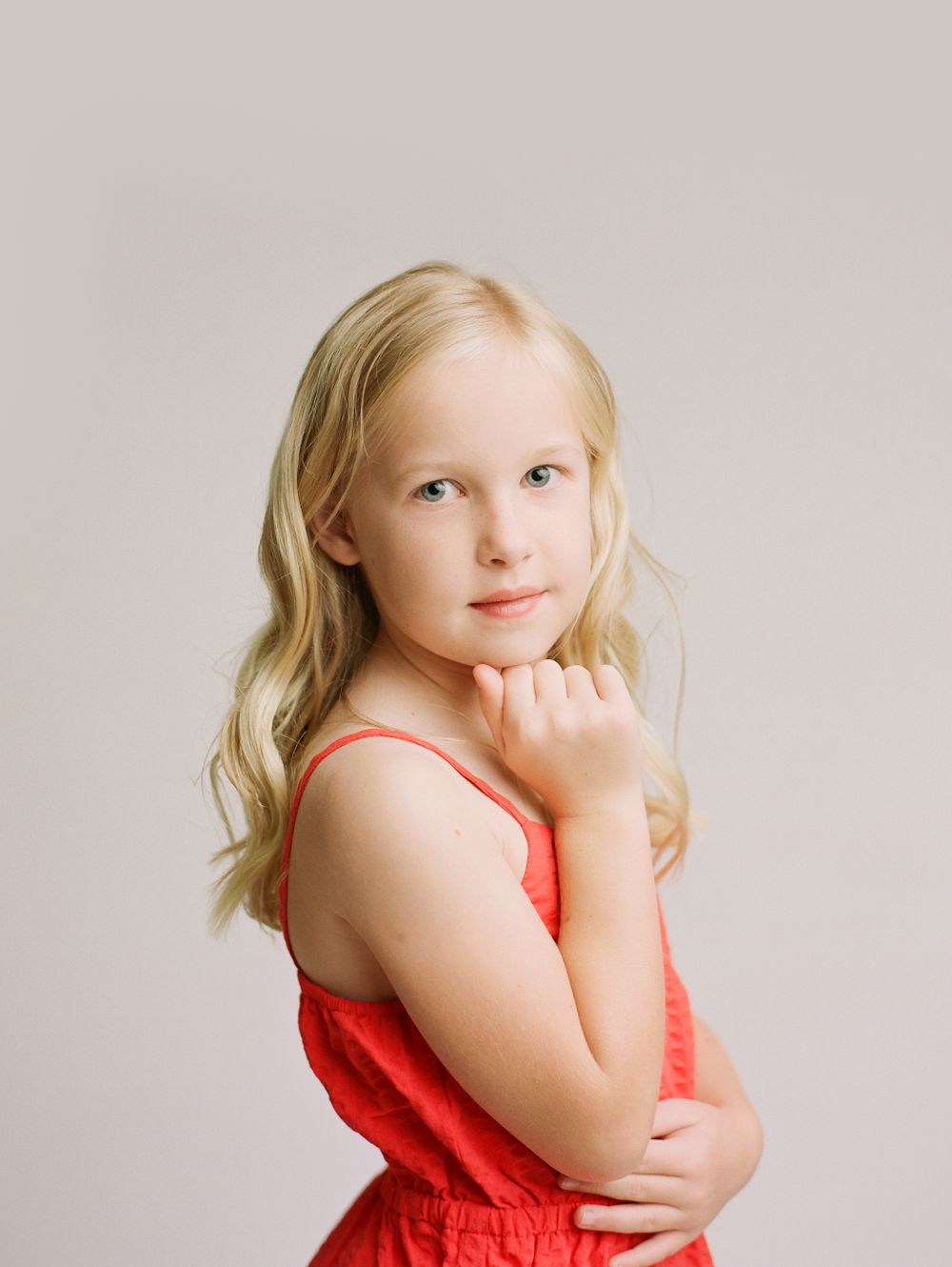 little girl in red strap summer dress looking at camera from side view with neutral background