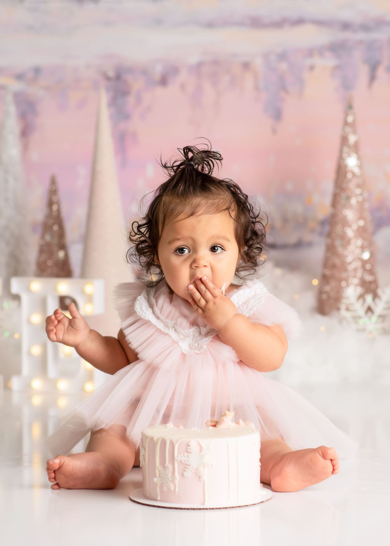 a baby gently puts cake in her mouth at her smash cake winter onederland