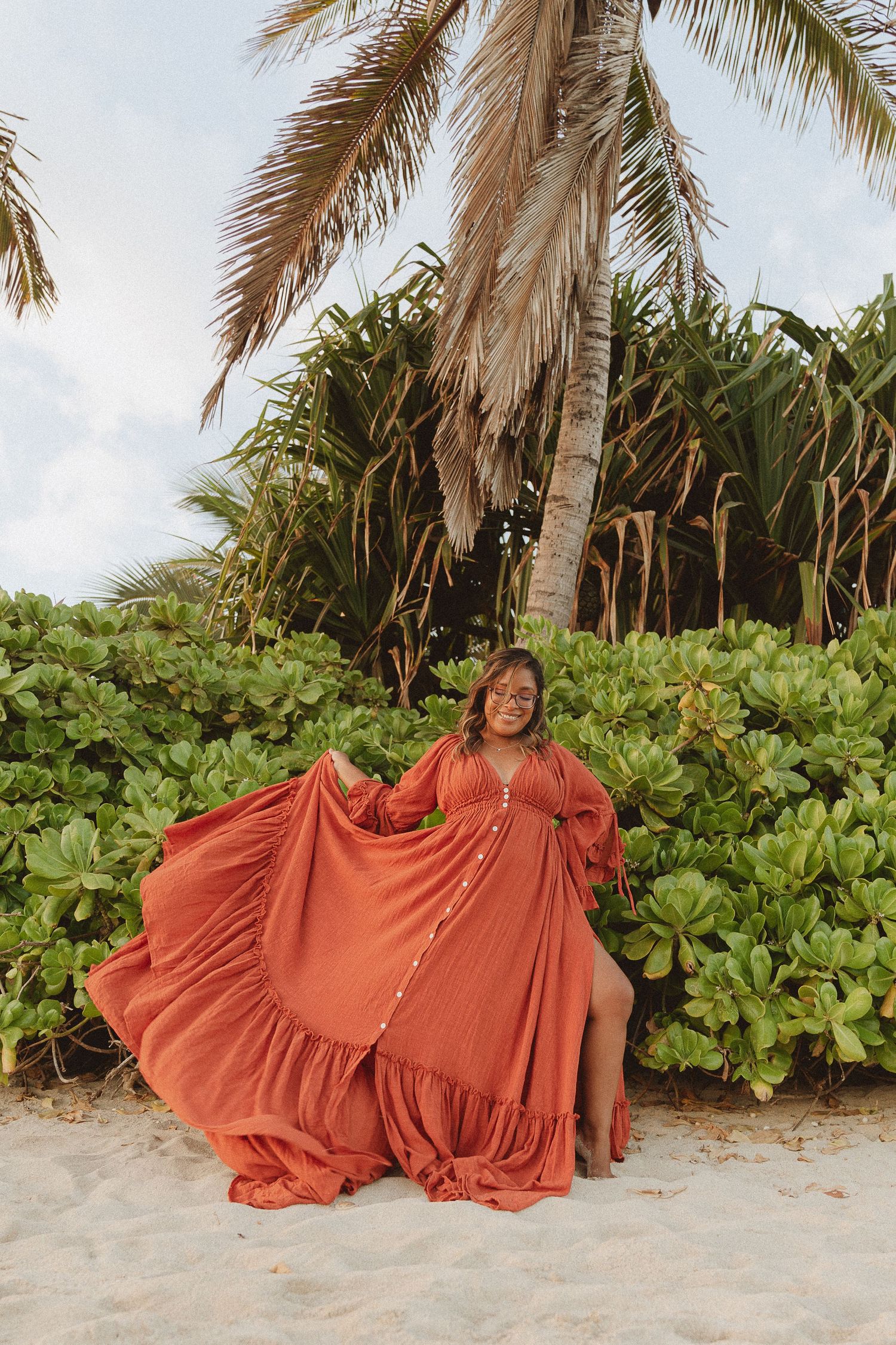 Photographer Kelly Pagan of Moments With Kell posing on the beach with her burnt orange dress on Oahu in Hawaii