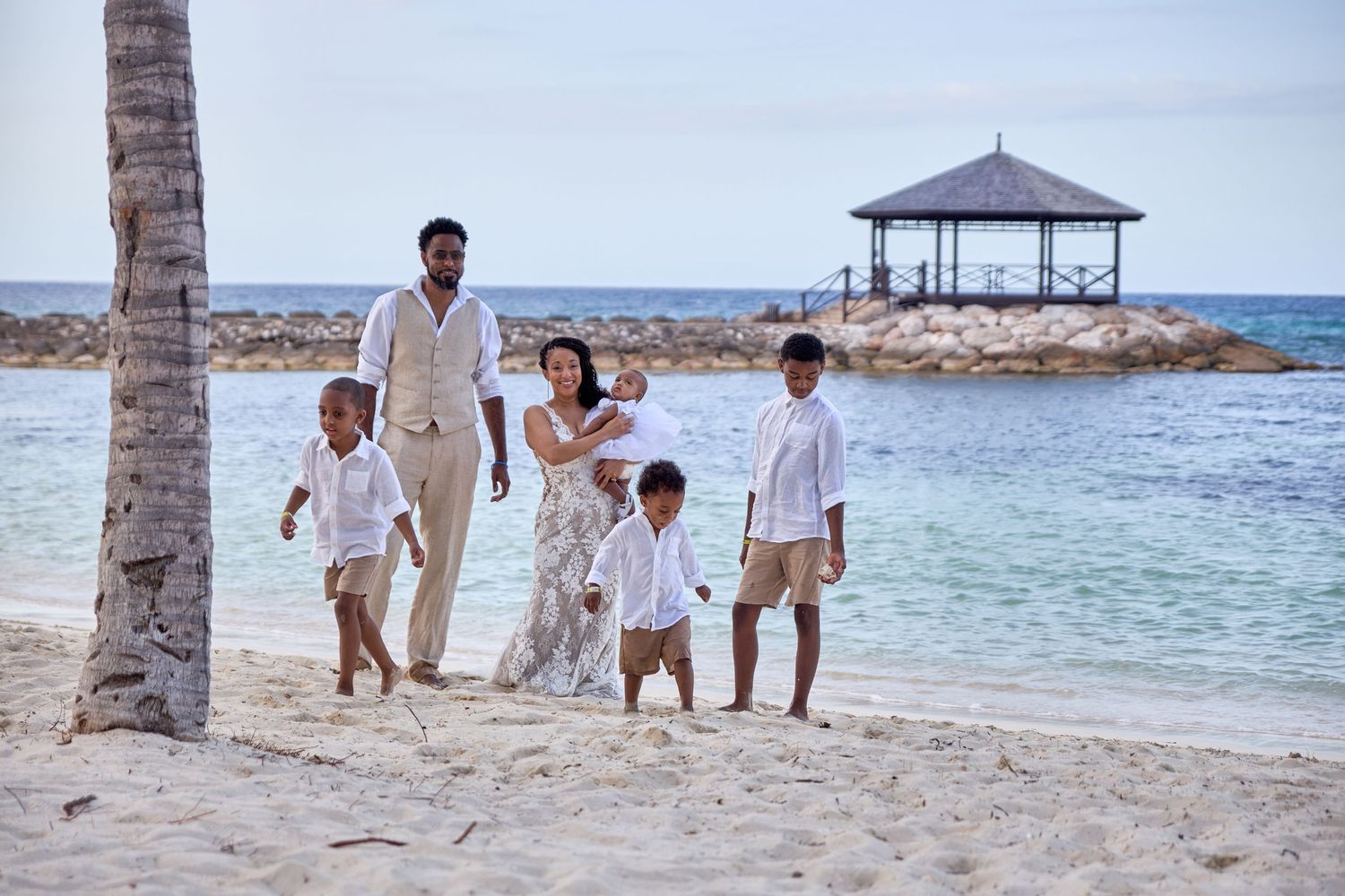 Beach photoshoot with family members in white outfits near ocean.