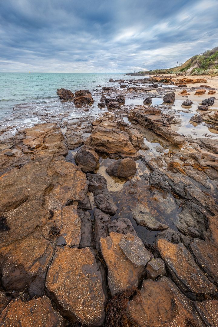 Rocky coastal landscape with turquoise water and cloudy sky stretching to distant headland.