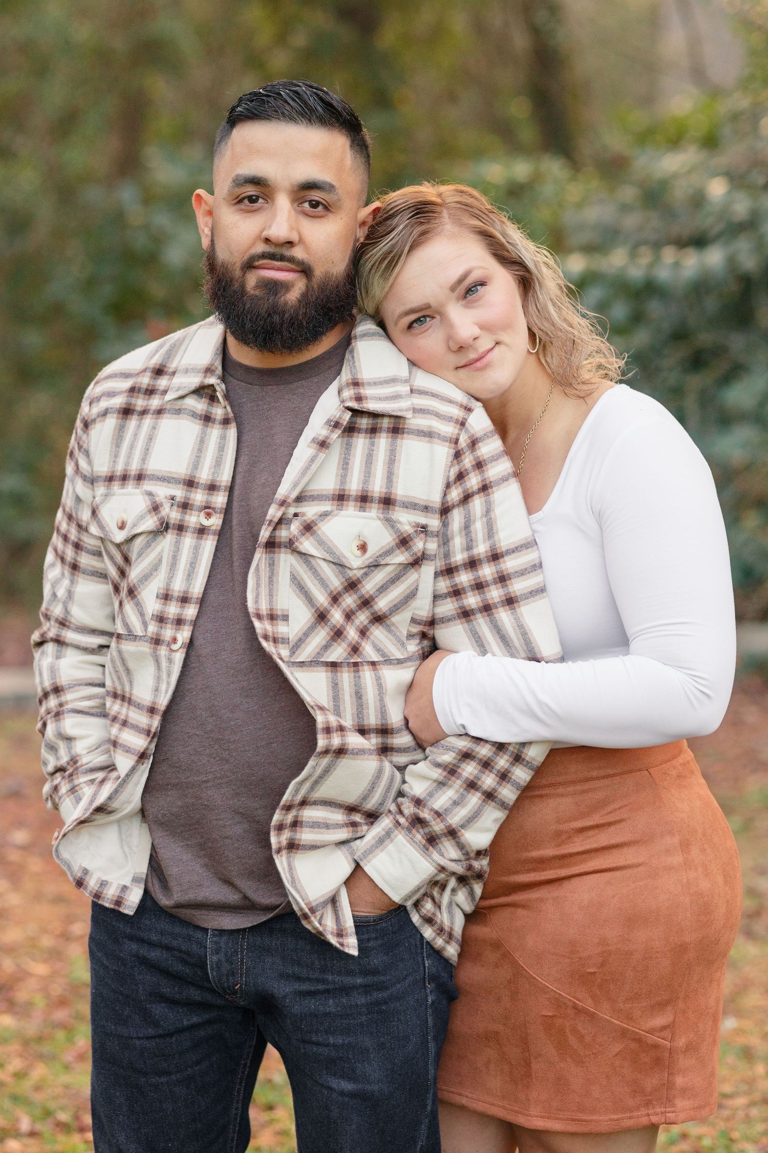 Couple poses for a portrait wearing complementary casual outfits in an autumn setting.