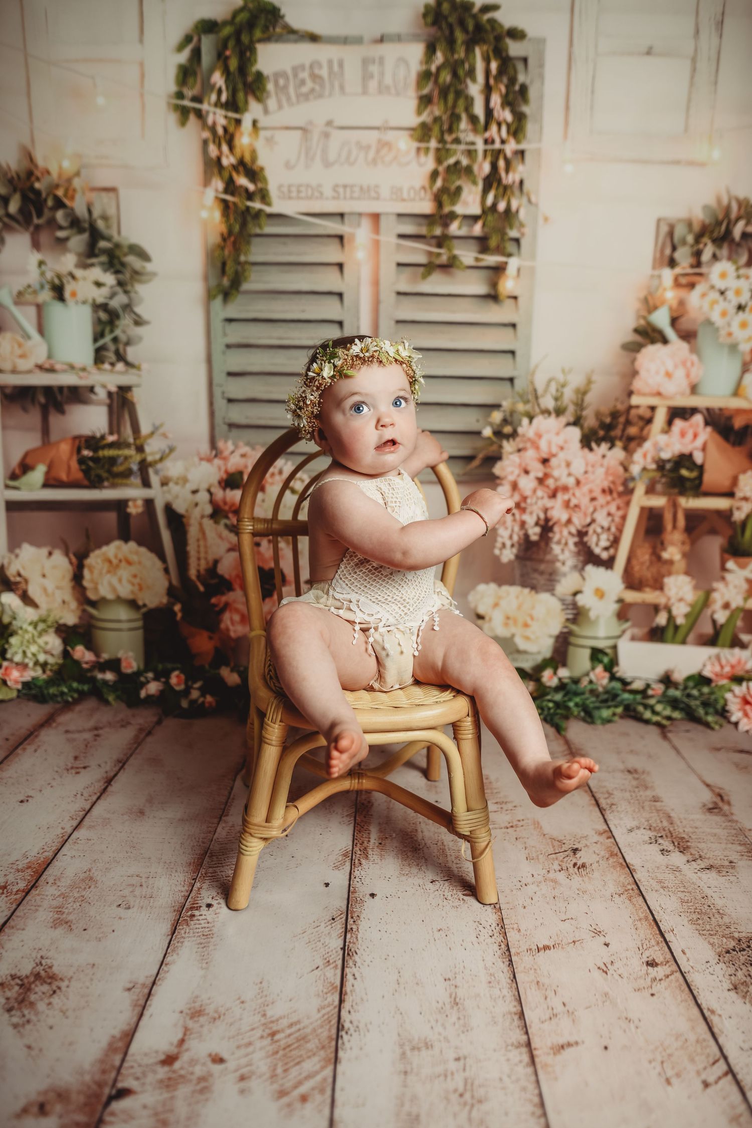 Baby sitting on vintage wooden chair in rustic setting with floral decorations.