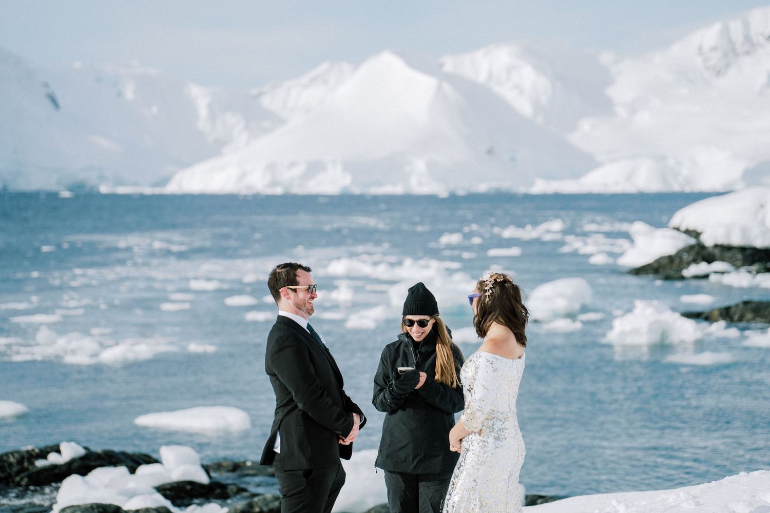 Wedding ceremony on snowy Antarctic shore with mountains and floating ice in background.