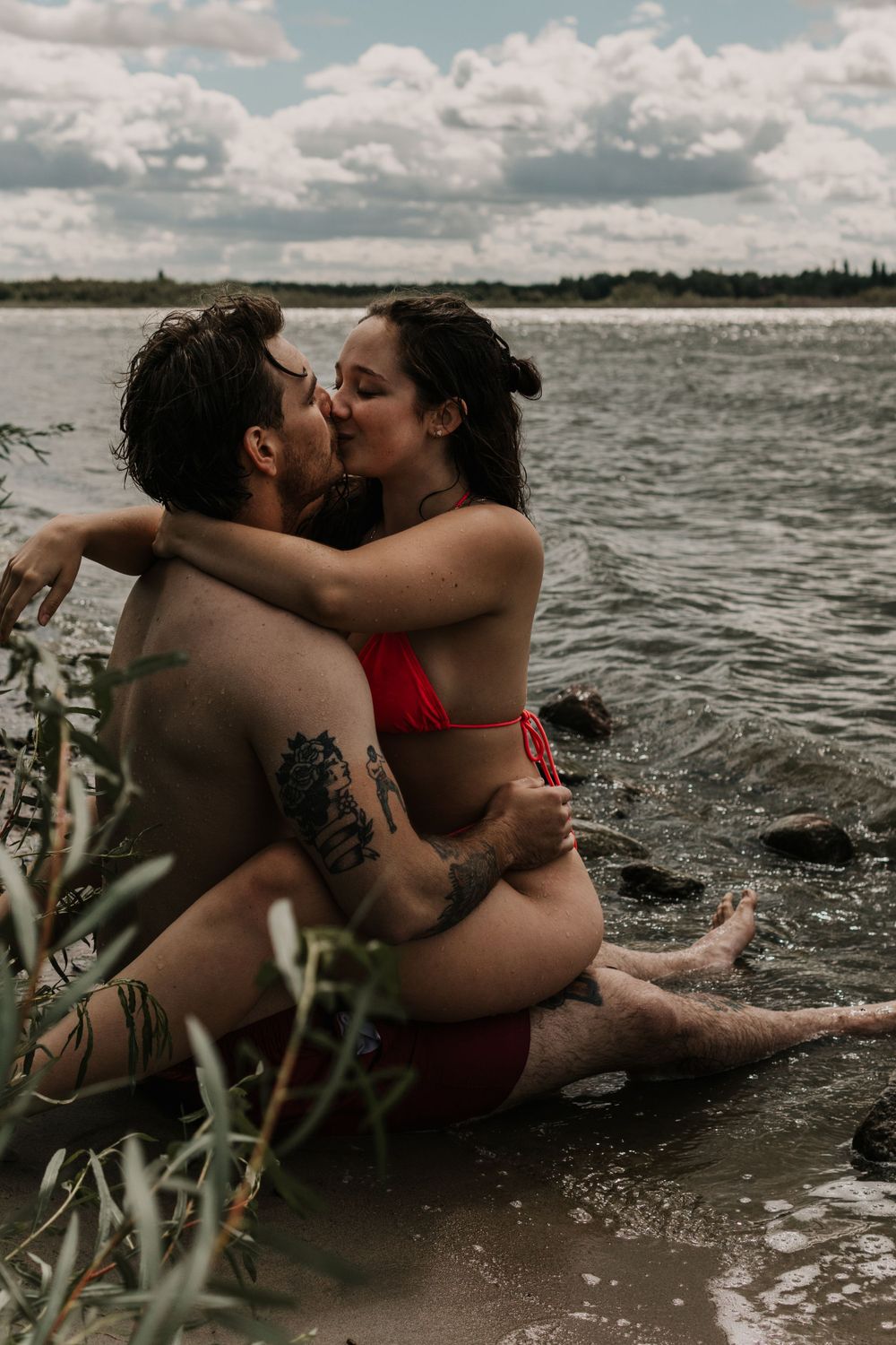 Couple's photoshoot at lakeside with dramatic cloudy sky and natural elements.