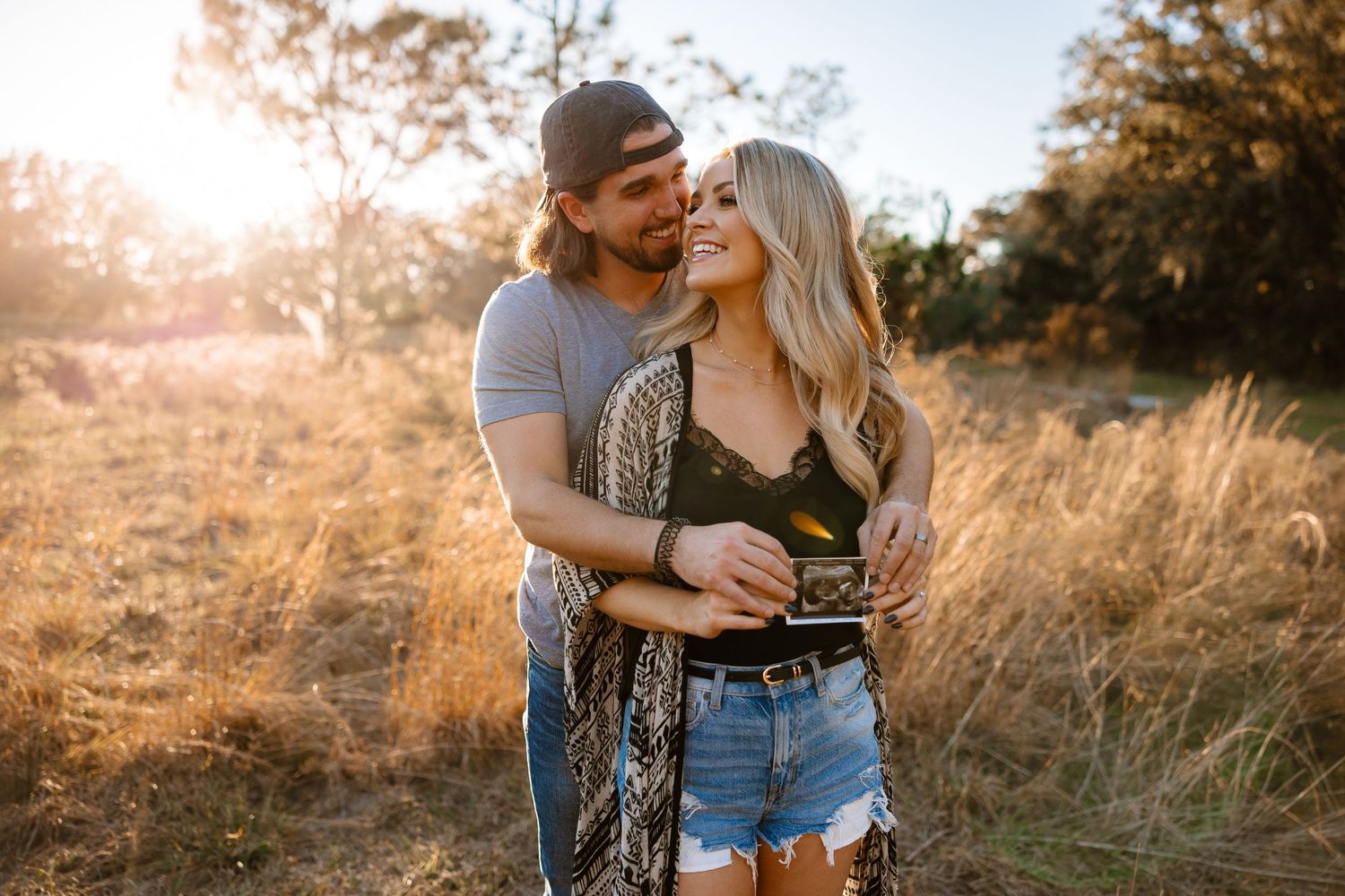 Young couple embracing and smiling in a golden field during a warm autumn sunset.