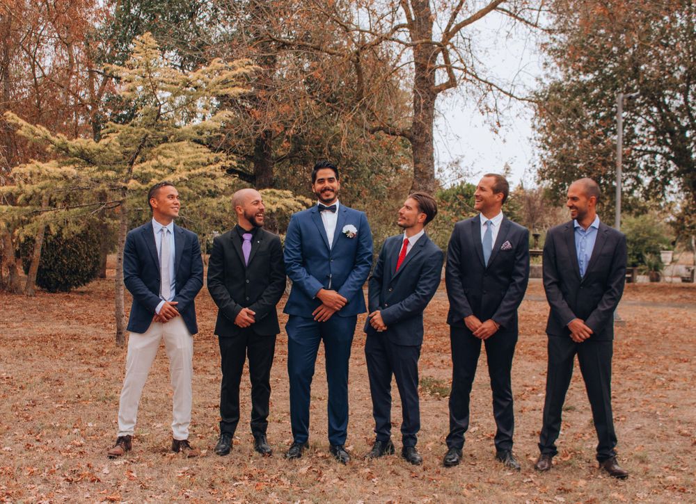 Groomsmen in coordinated suits and blazers pose together at an outdoor autumn wedding.
