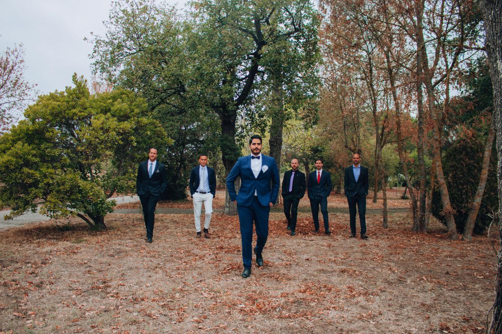 Wedding party walking through fall foliage with groom in blue suit leading the group.