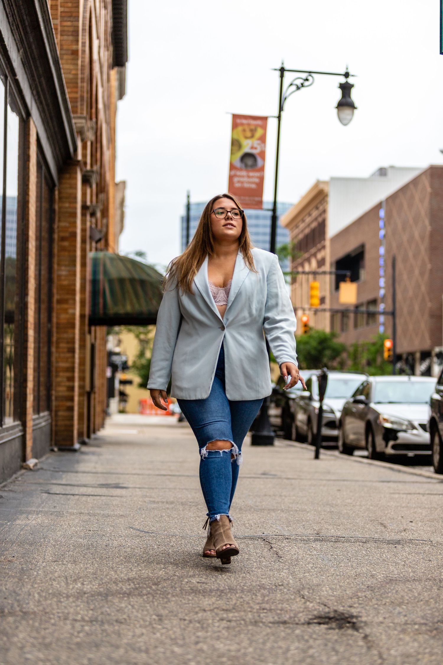 Stylish woman in grey blazer and ripped jeans walking confidently down urban city sidewalk.