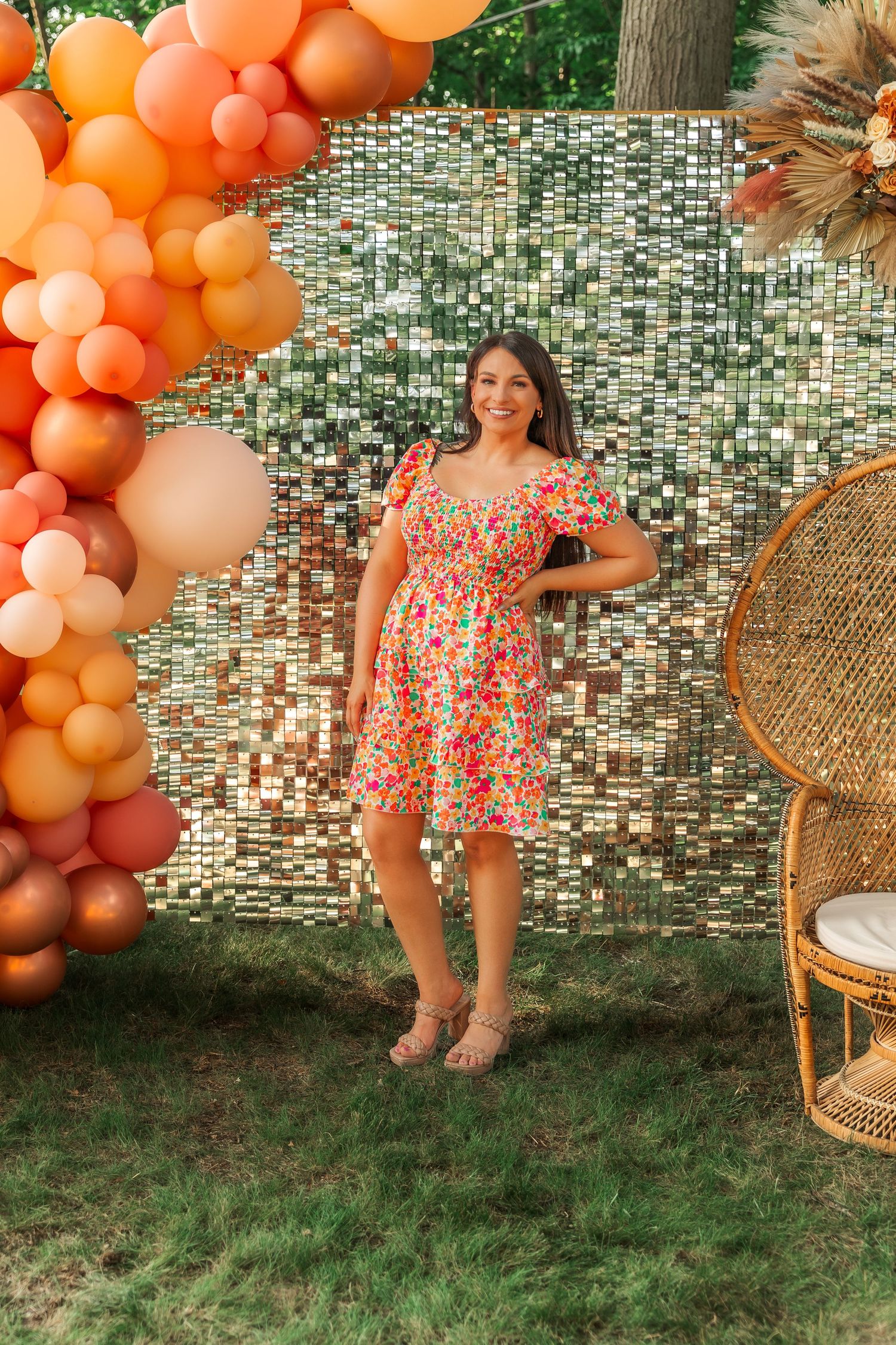 Coral balloon arch and rattan chair create a festive backdrop for a floral dress photoshoot.