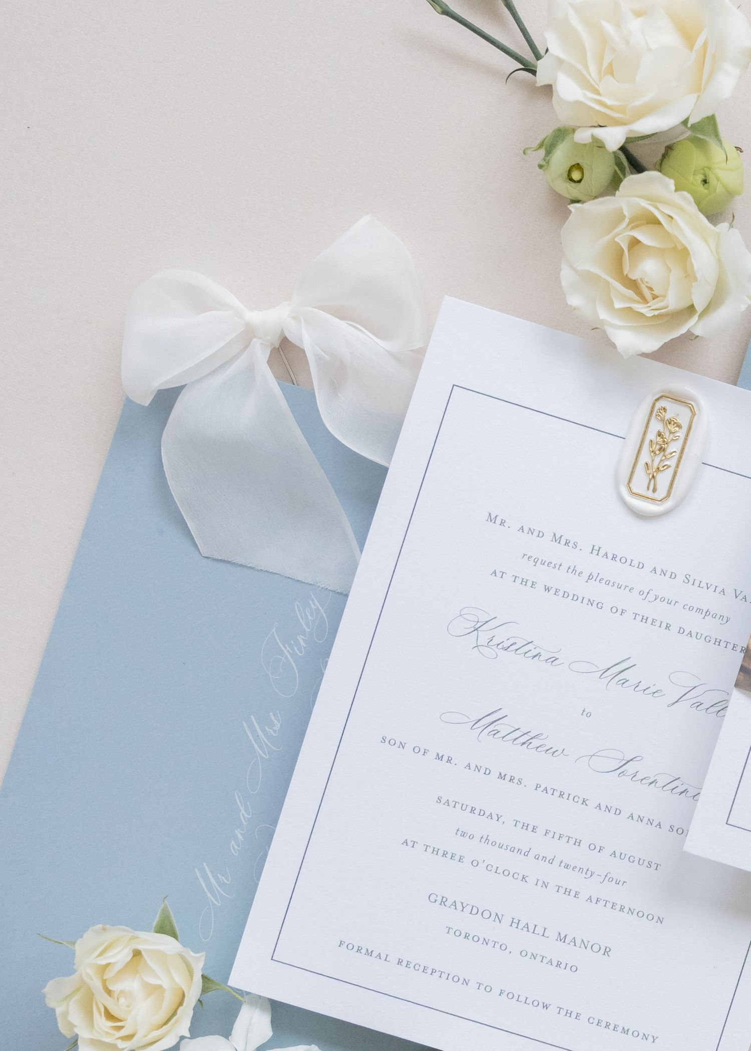 Elegant white wedding invitation with light blue envelope and white roses against neutral background.