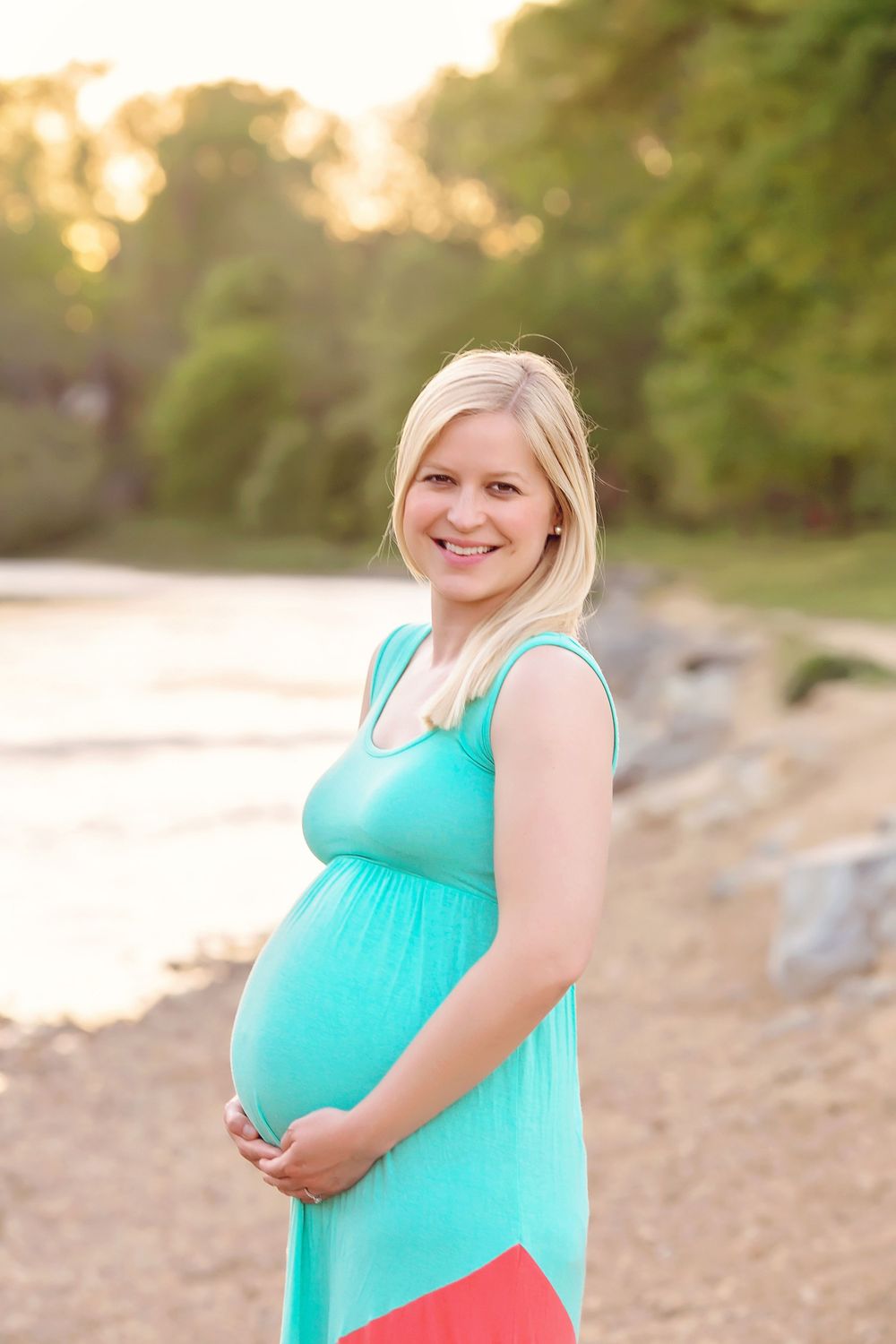 Person in turquoise dress poses on beach during sunset maternity photoshoot.