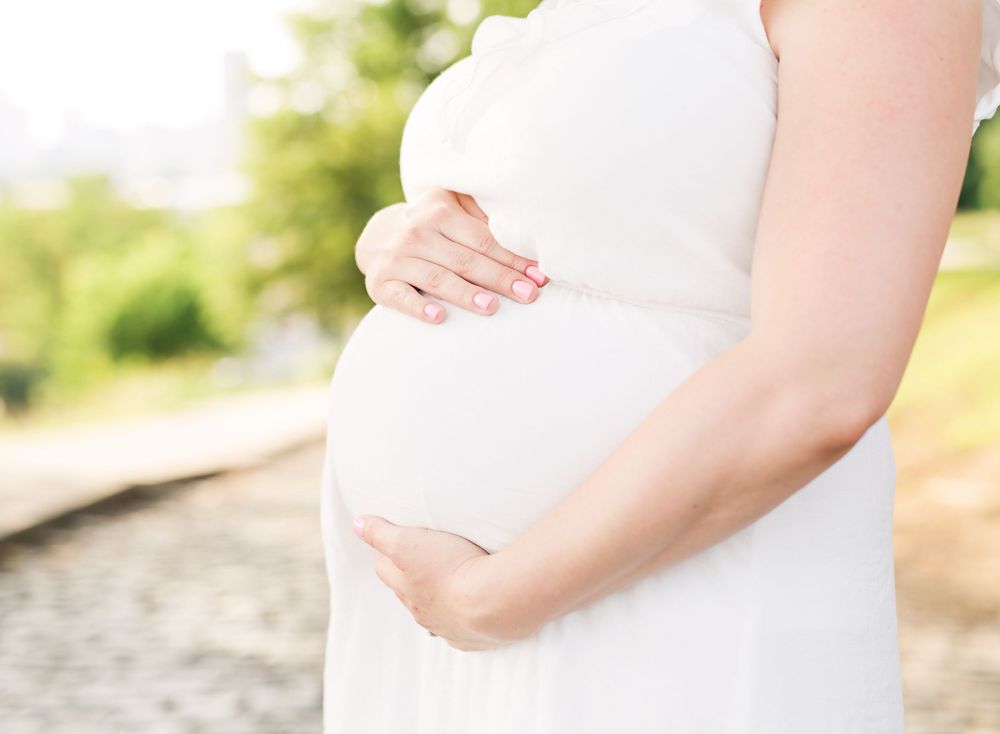 Close up of hands cradling pregnant belly in white maternity dress.