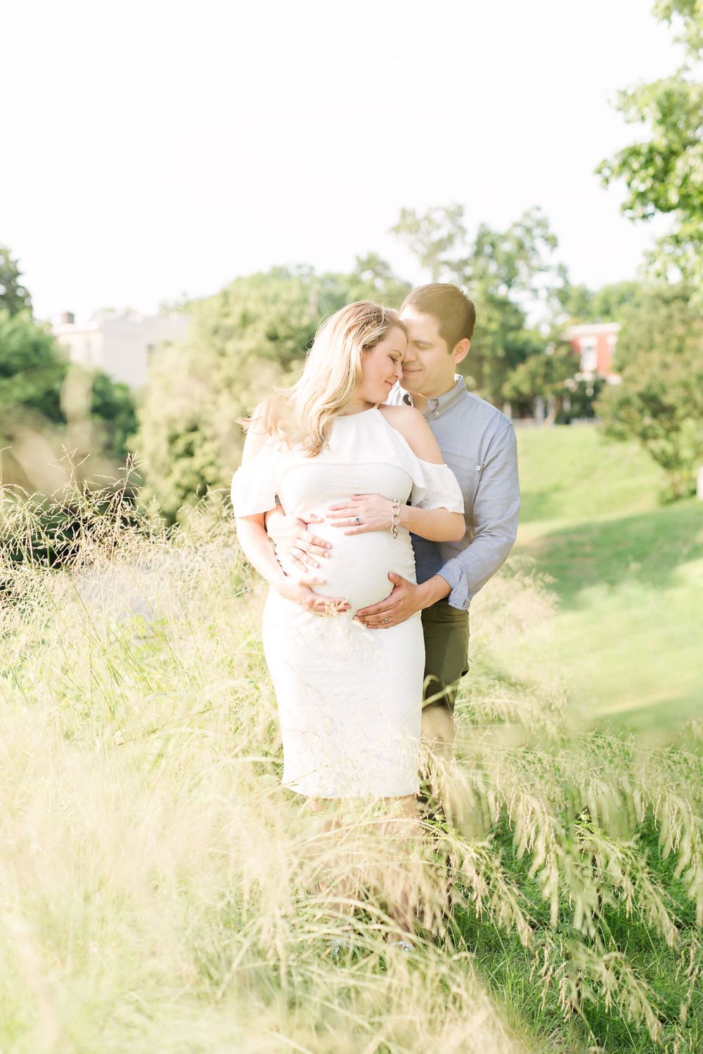 A romantic maternity photo of a couple embracing in tall grass during golden hour.