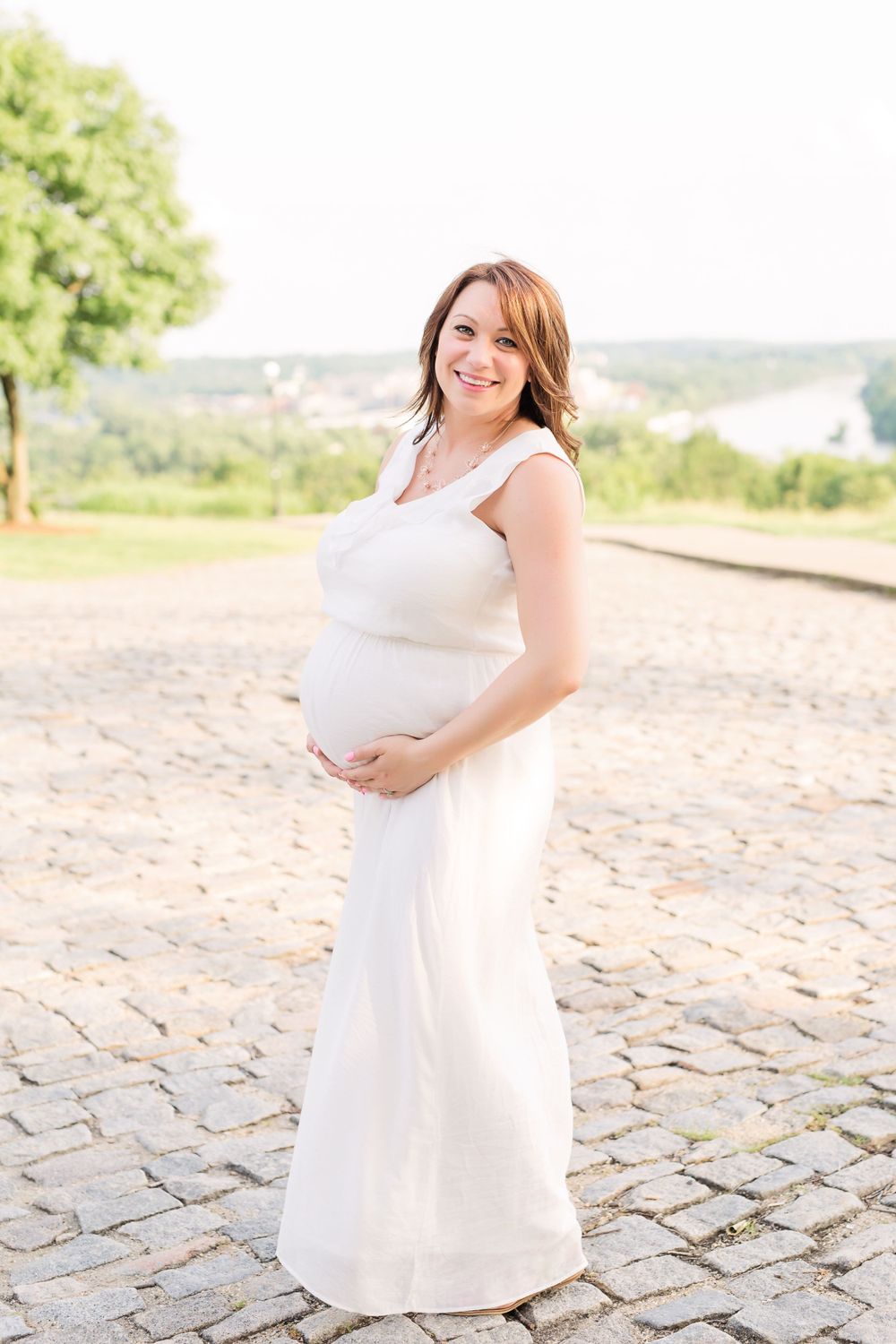 Person in white dress poses outdoors during maternity photoshoot.