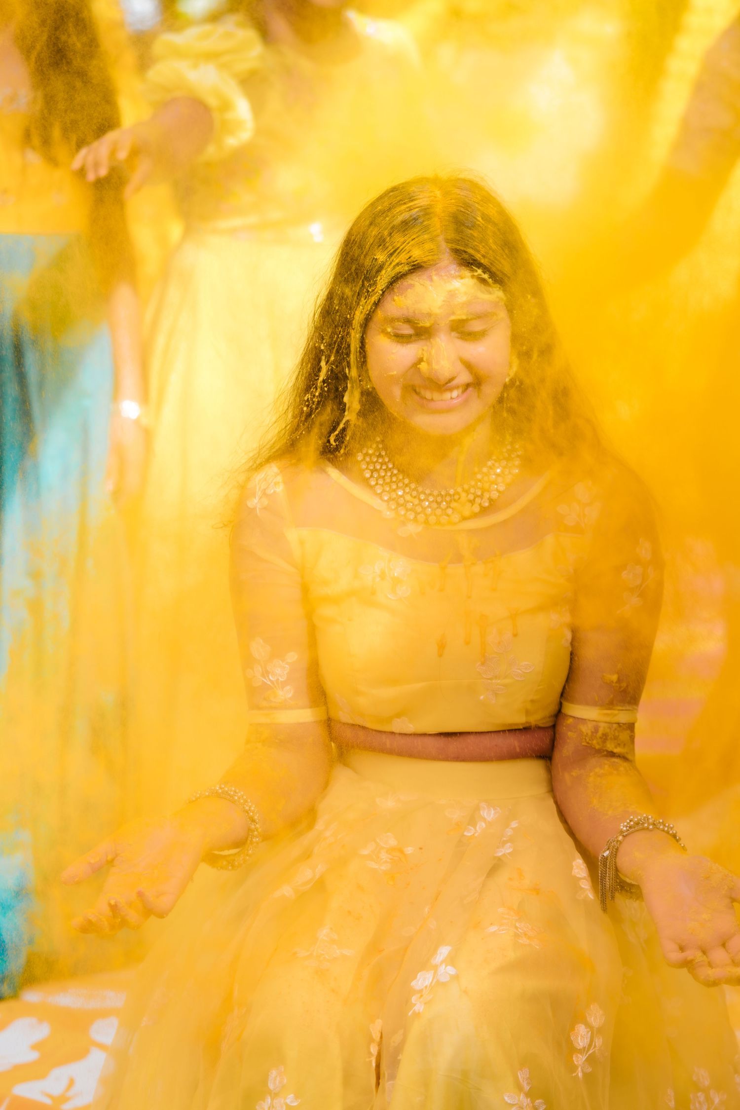 A woman wearing a yellow lehenga laughs joyfully during a traditional Haldi ceremony.