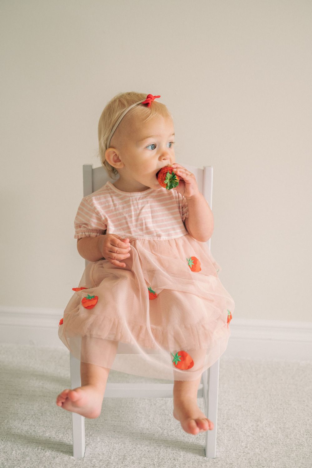 Pink dress with strawberry pattern on white chair against neutral background.