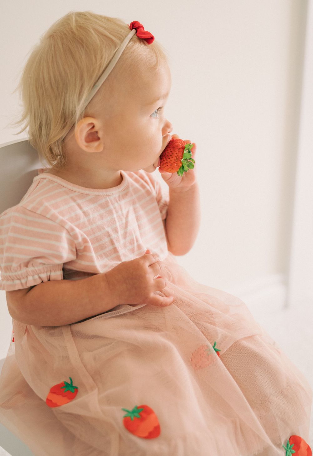 Side view of someone seated in white chair wearing pink dress with strawberry decorations.