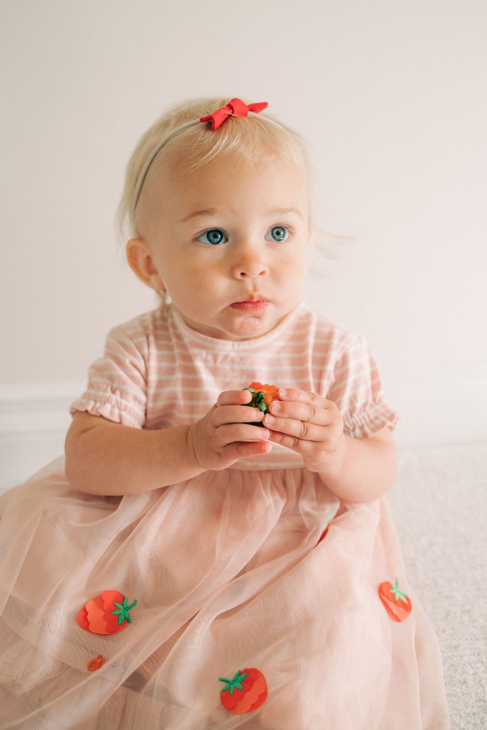Sweet moment captured in pink dress with strawberry decorations against light background.