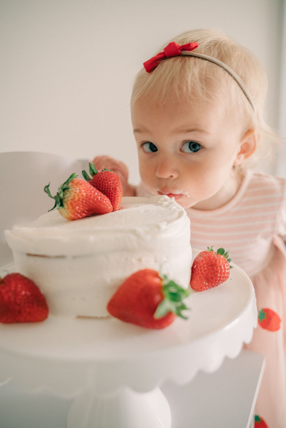 White tiered cake decorated with fresh strawberries on elegant cake stand.
