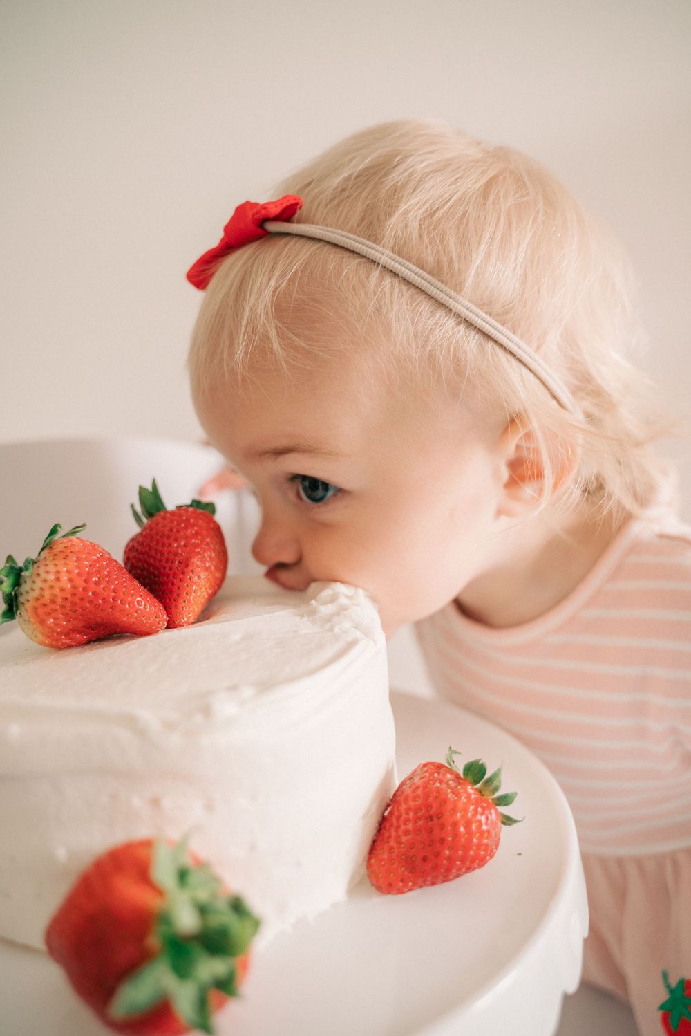 Fresh strawberries adorning white frosted cake on display stand.
