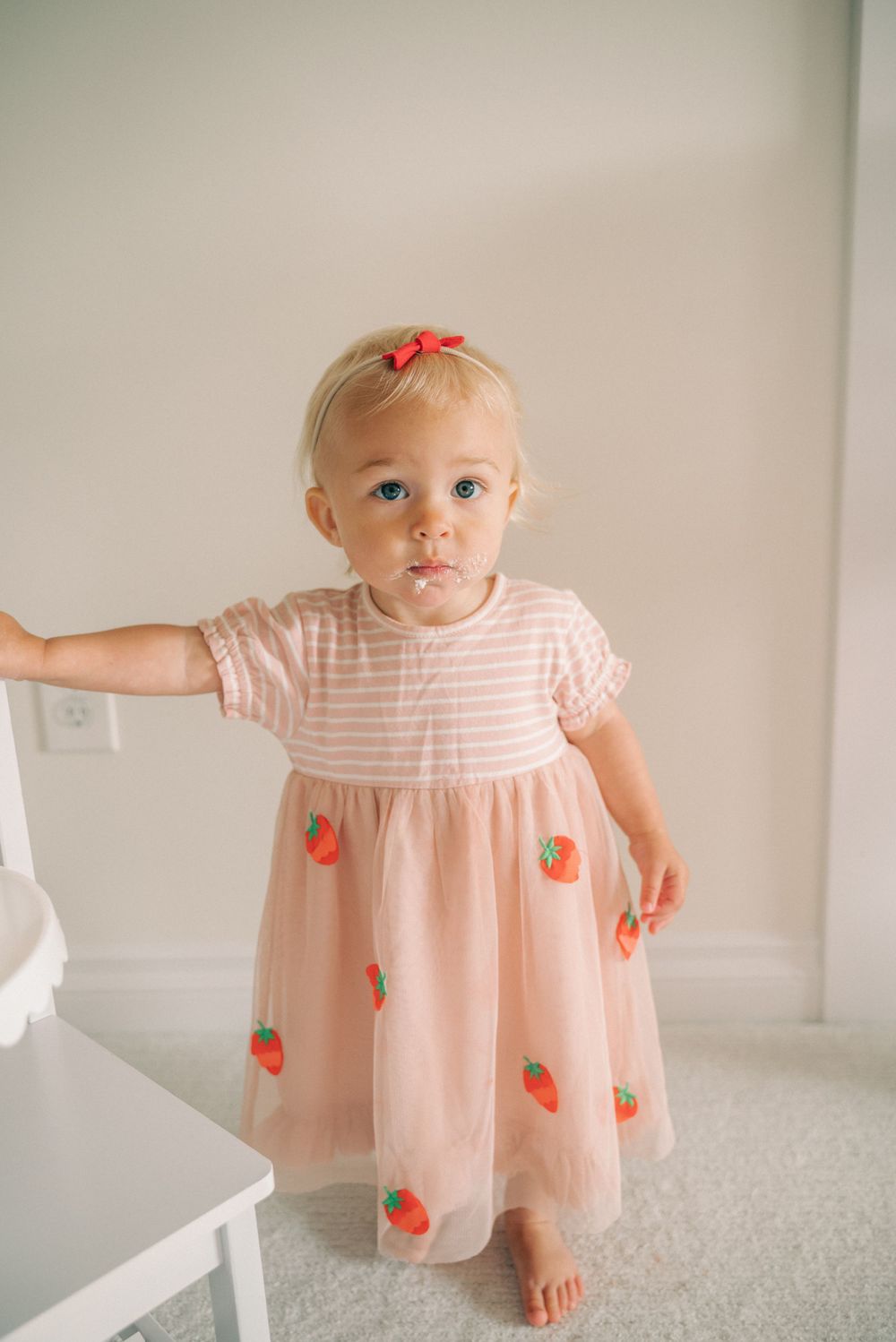 Full length view of pink strawberry-patterned dress against neutral wall.