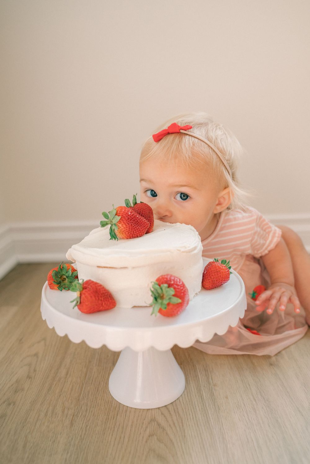 A white tiered cake decorated with fresh strawberries on a pedestal stand with someone reaching toward it.