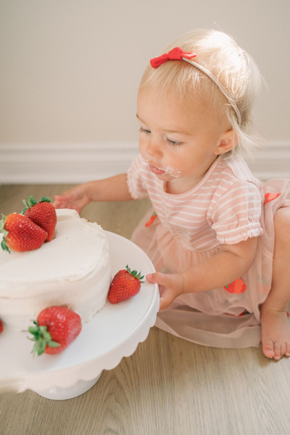 A beautifully decorated white cake with fresh strawberries on a white cake stand.
