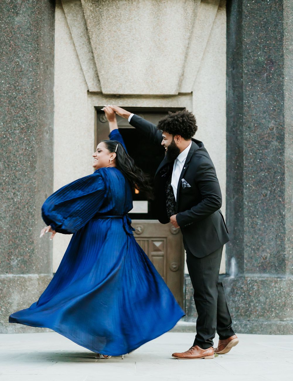 Couple dancing with dramatic blue dress flowing in front of historic building entrance.