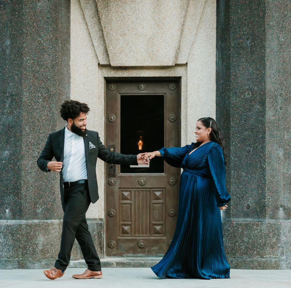 Couple in formal attire dancing playfully in front of an ornate wooden door.