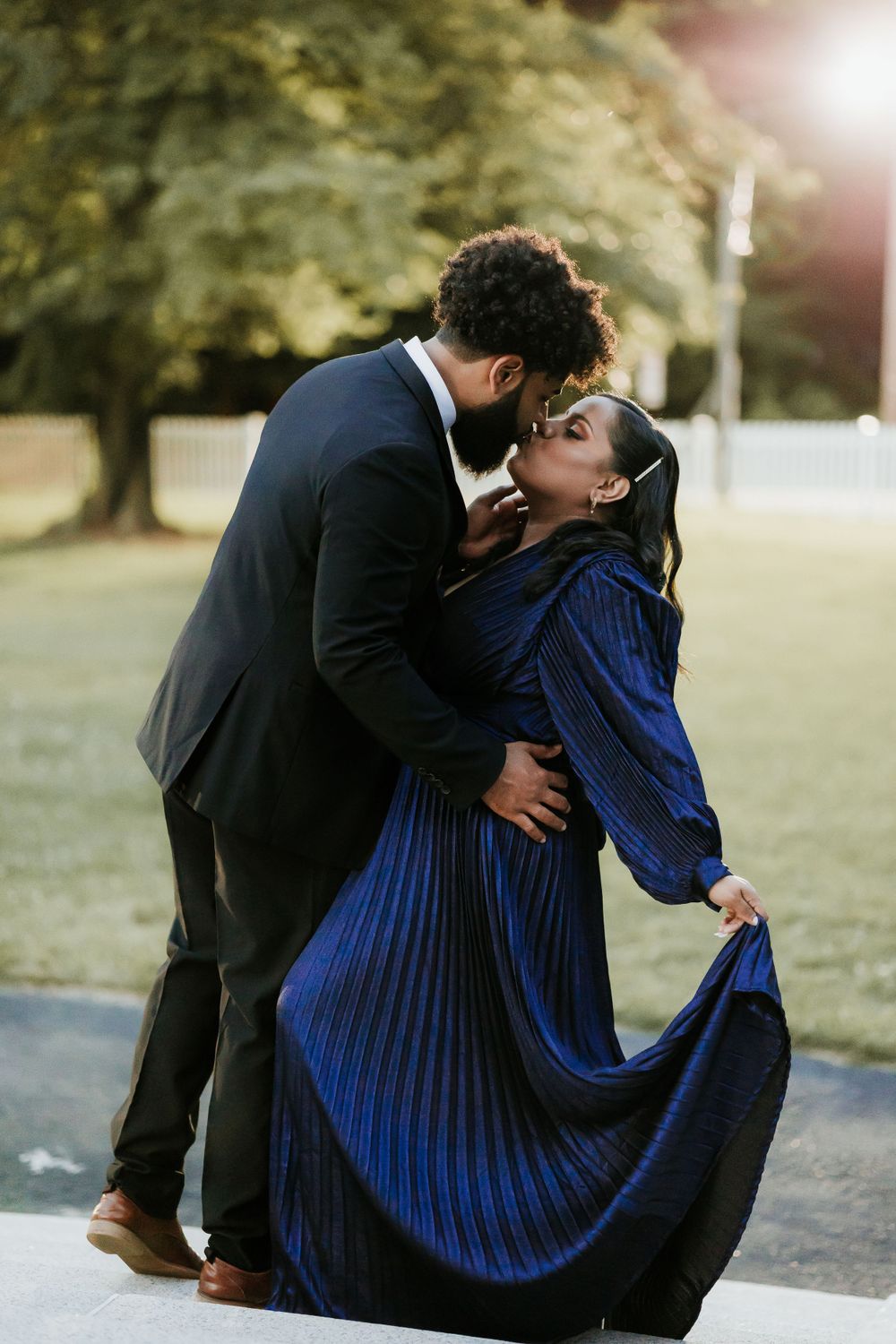 Romantic couple sharing a tender moment in formal attire against a sunlit outdoor backdrop.