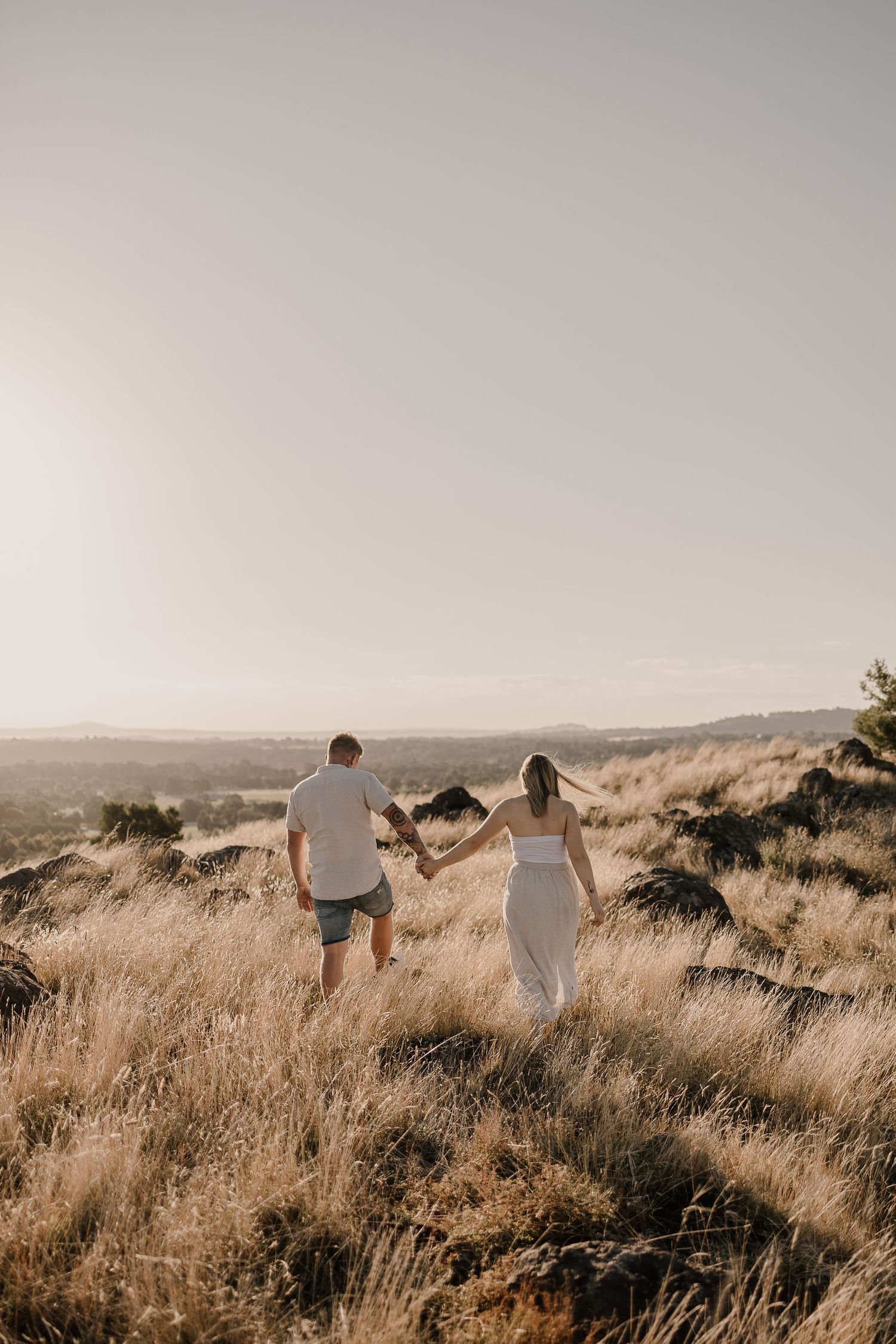 Two people walk hand in hand along a scenic hilltop trail at sunset.