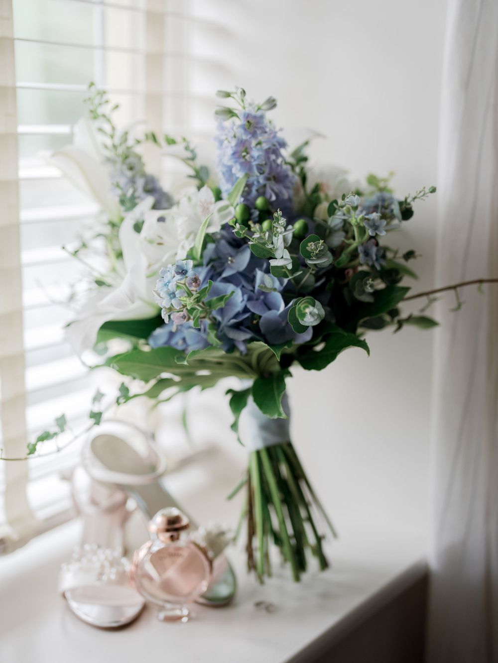 Delicate blue and white wedding bouquet with hydrangeas displayed beside bridal accessories.