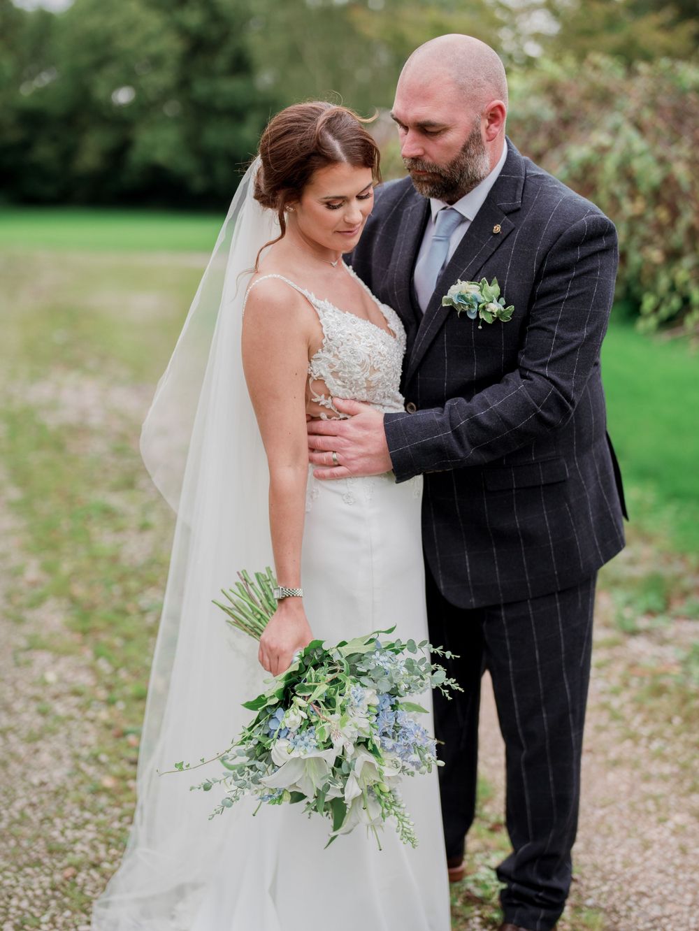 Intimate outdoor portrait of newlyweds embracing against garden backdrop.