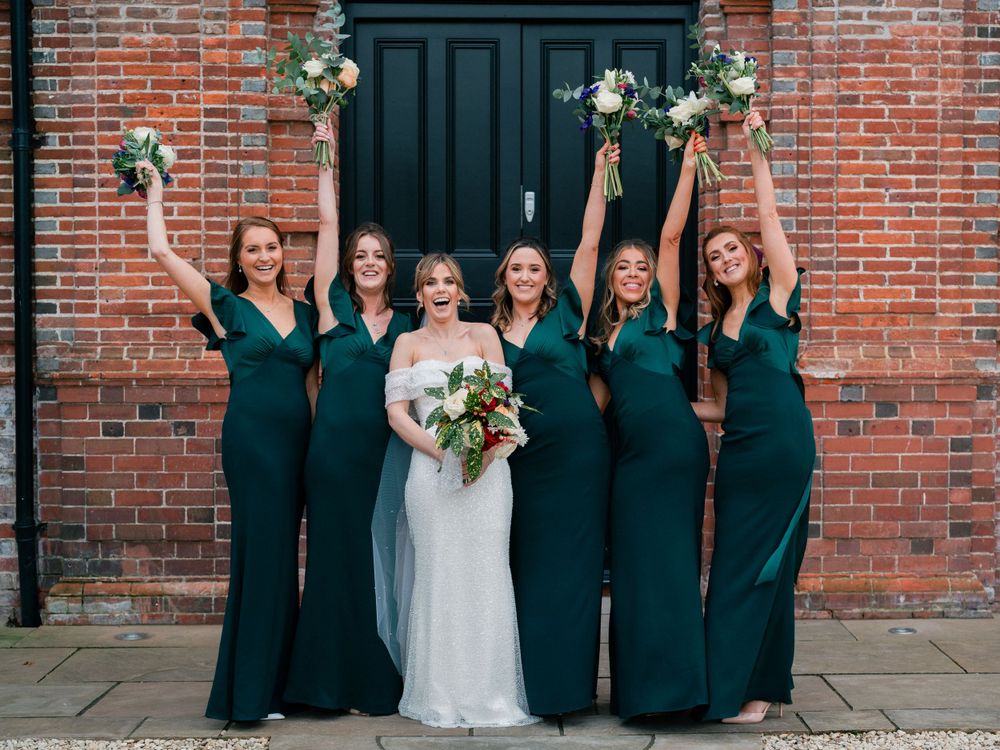 Wedding party in navy blue dresses poses against brick wall exterior.