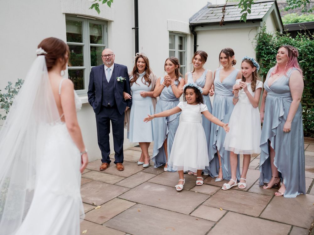 Wedding party in light blue dresses reacts with joy to seeing the bride.