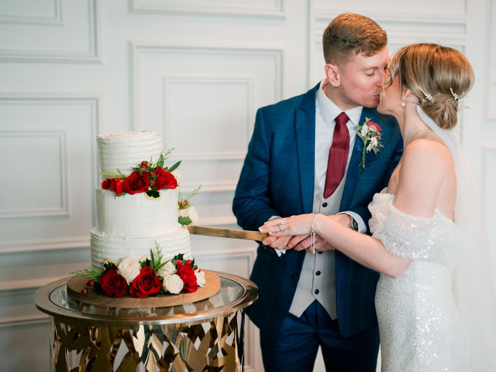 Wedding cake cutting moment on gold table against white paneled wall.