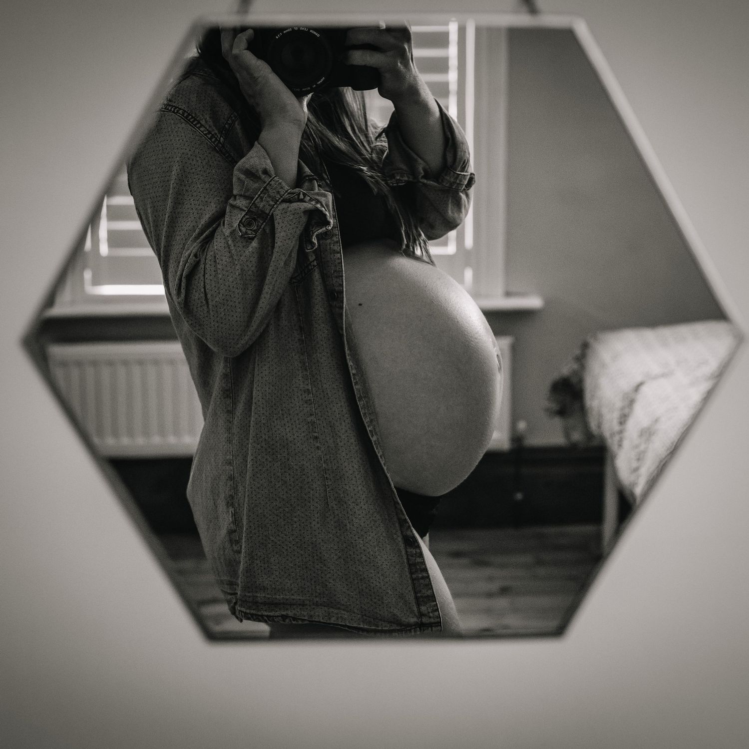 A black and white mirror selfie showing a pregnant belly in casual clothing.