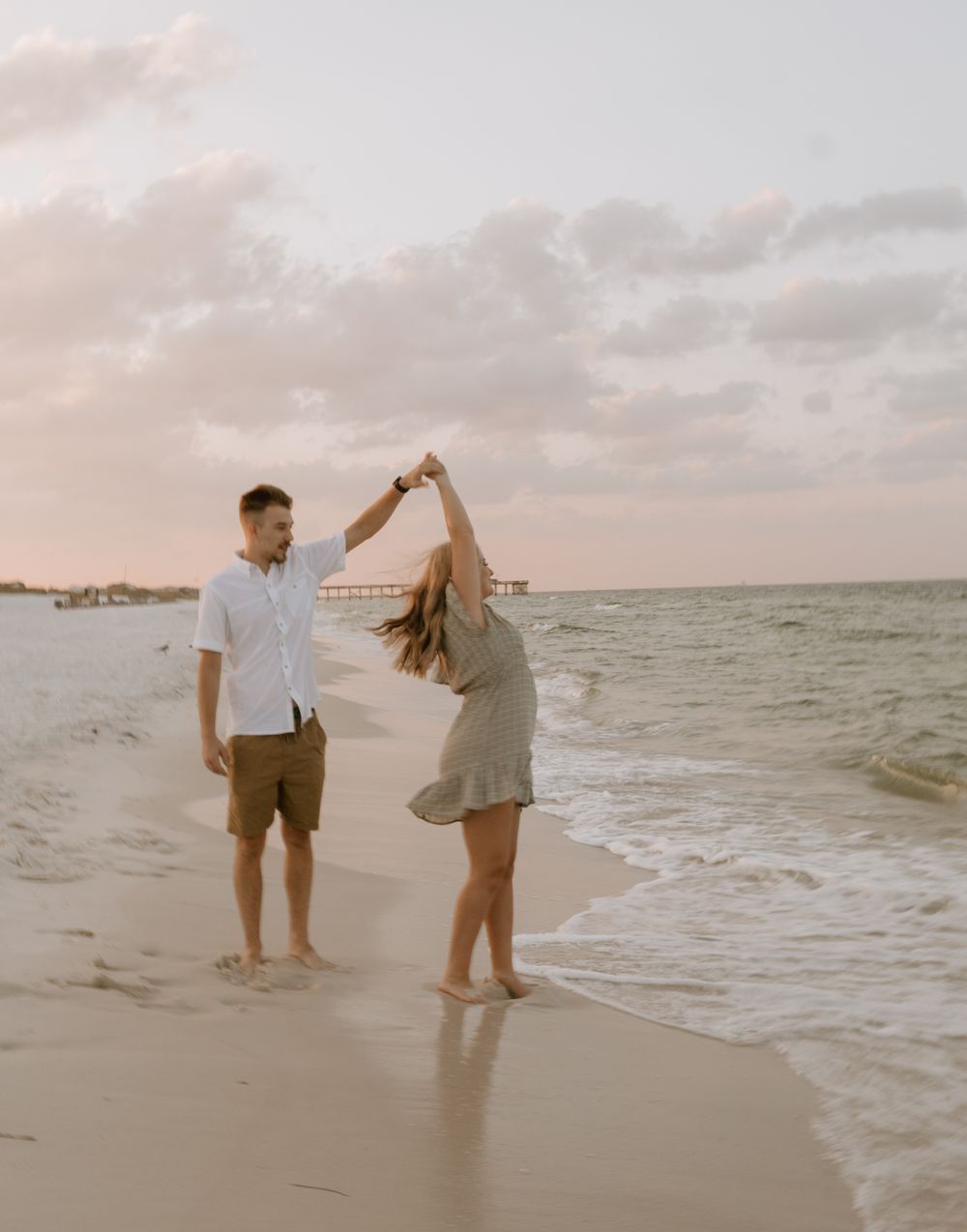 A couple dances together on a beach at sunset with waves in the background.