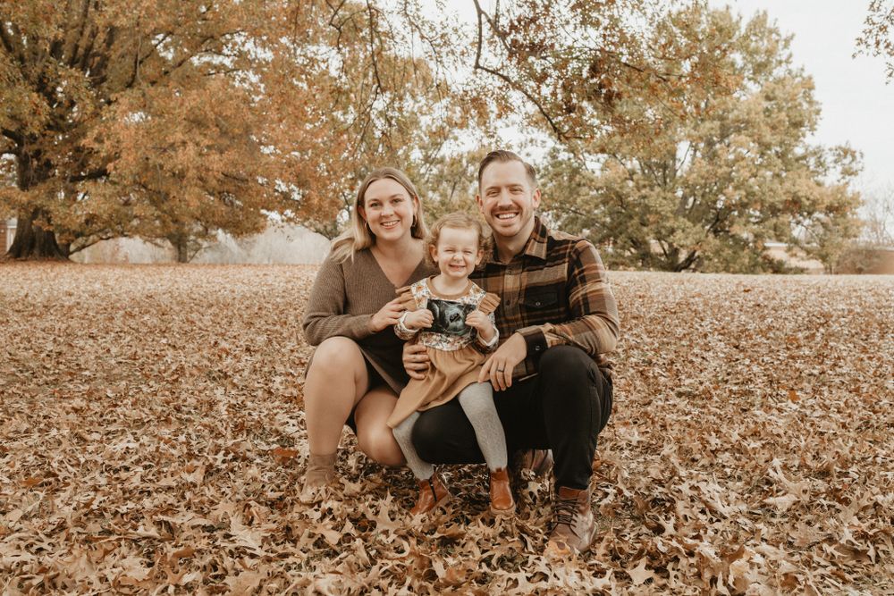 A family sitting together on fallen autumn leaves in a park setting.