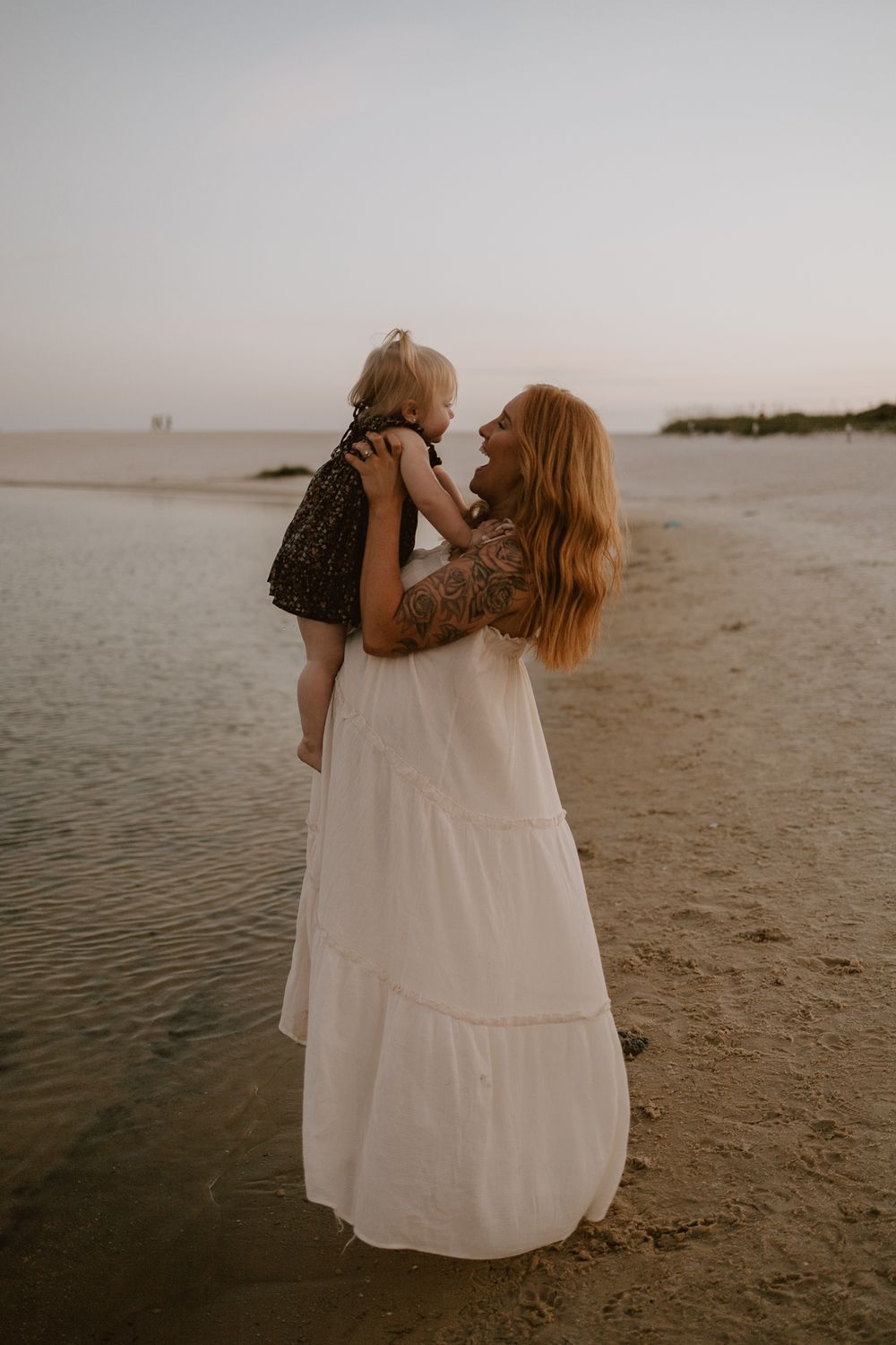 A touching moment between parent and child playing on a sandy beach at sunset.