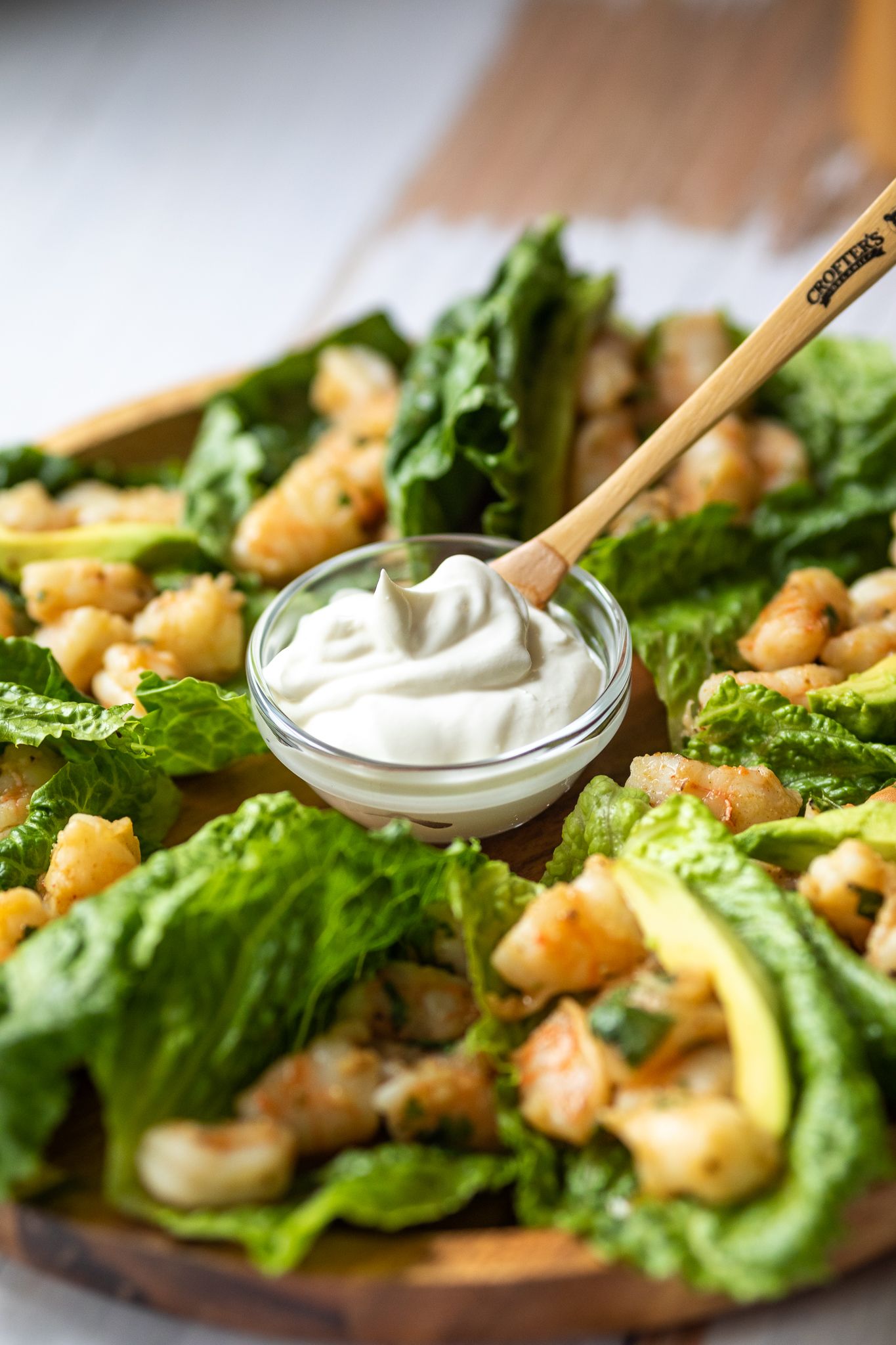 Crisp lettuce wraps with creamy sauce and garnishes served on a wooden board.