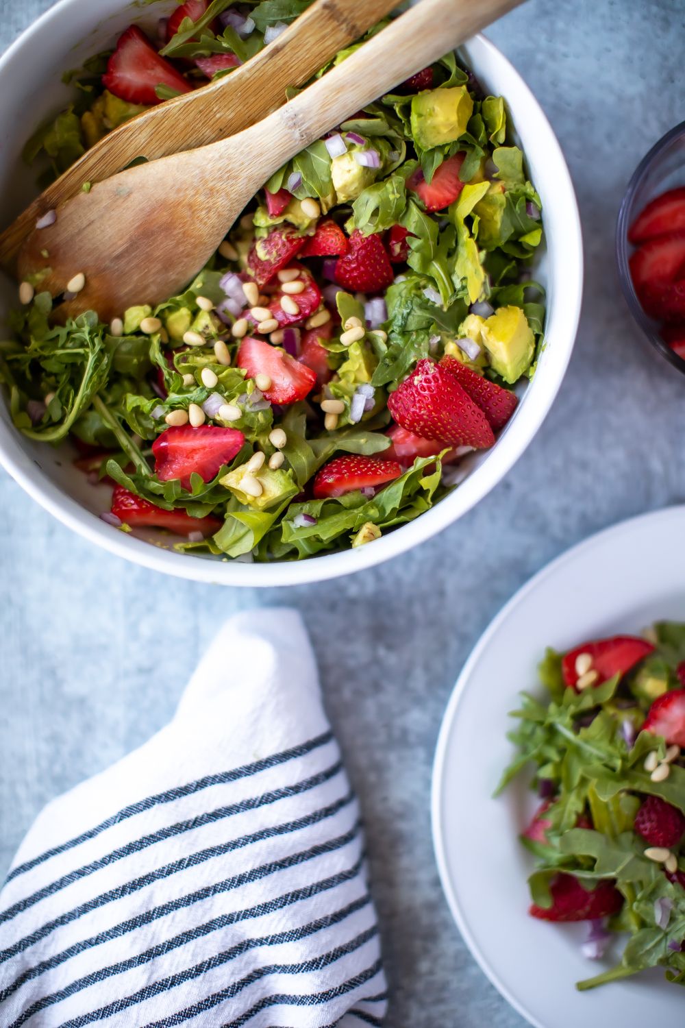 Colorful summer salad with fresh strawberries, avocado and mixed greens in a white bowl.