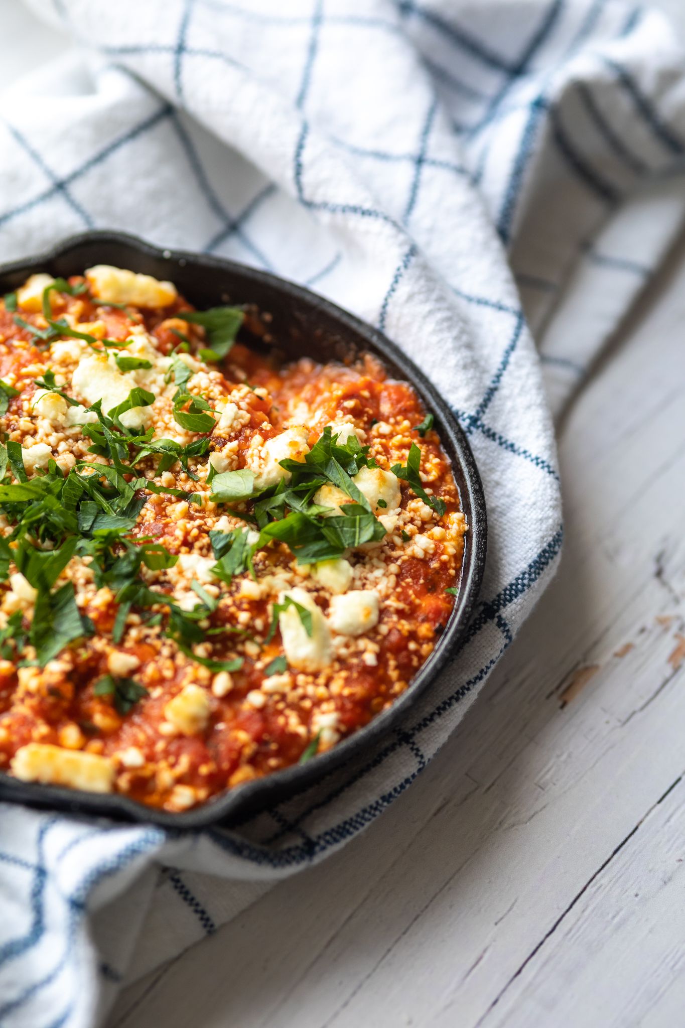 A skillet of baked feta pasta garnished with fresh herbs on a white striped cloth.