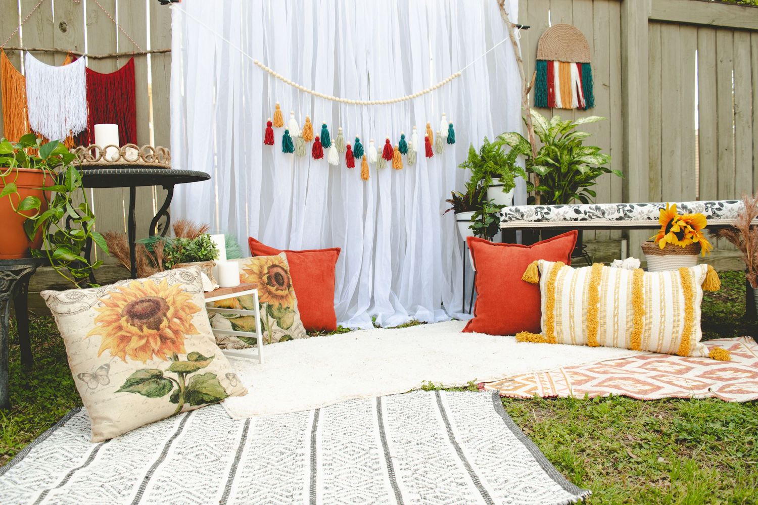 Outdoor party setup with colorful pillows, tassels and boho decorations against white backdrop.