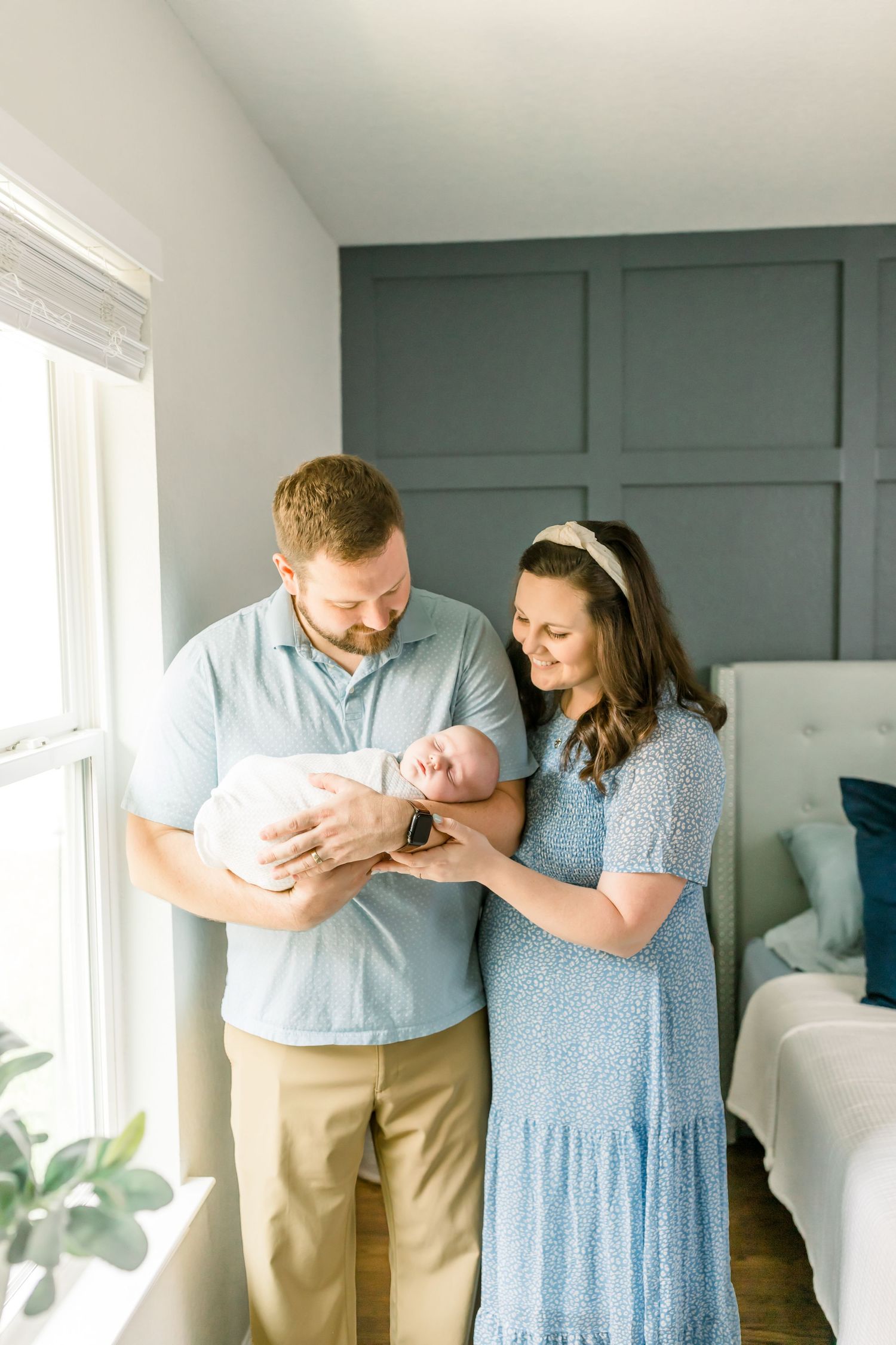 A tender family moment captured in a nursery with soft natural light and grey wall panels.