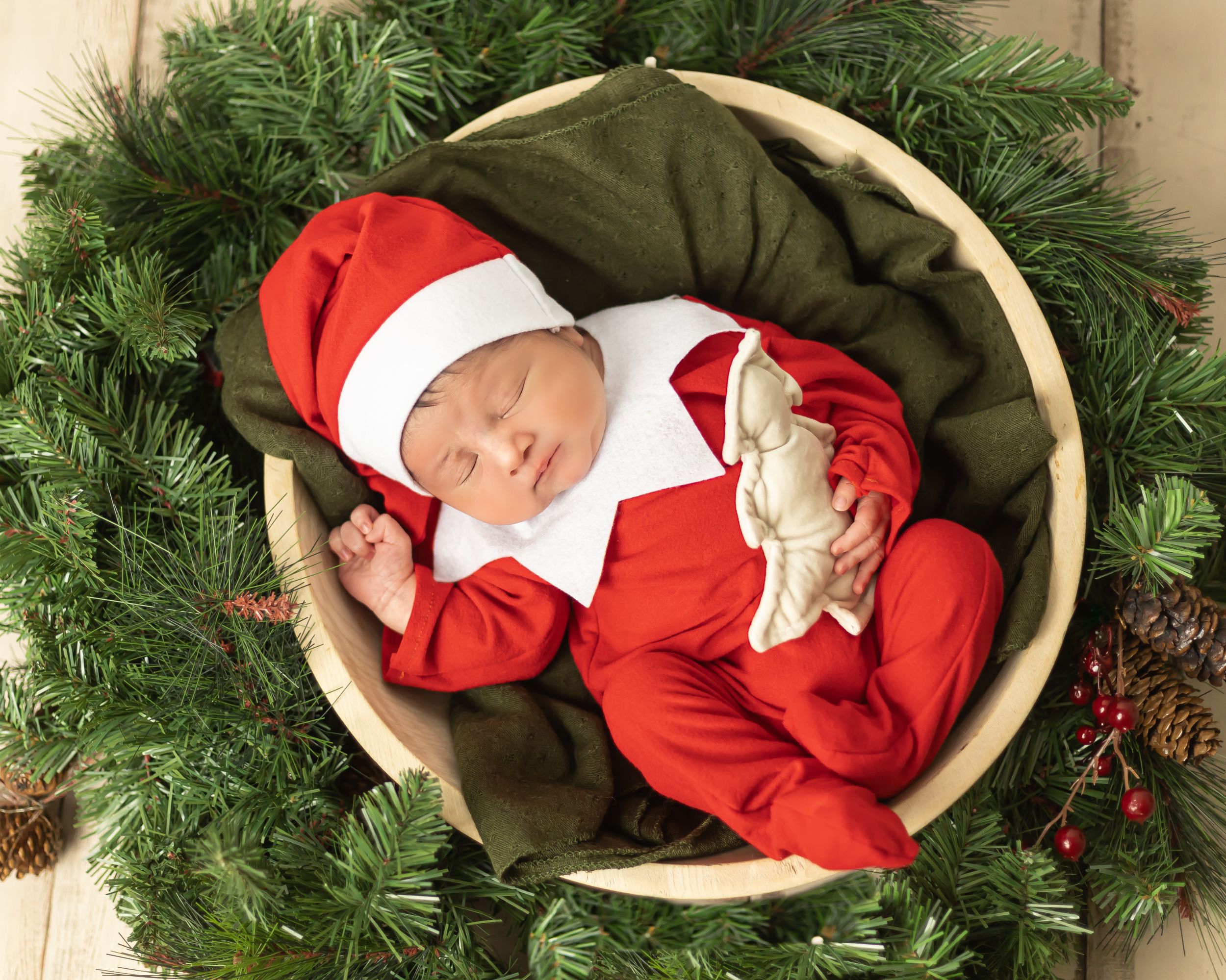 Sleeping baby in Santa outfit nestled in festive holiday wreath setting.