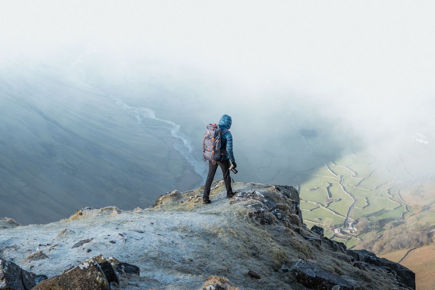 Hiker standing on rocky mountain peak overlooking misty valley below.