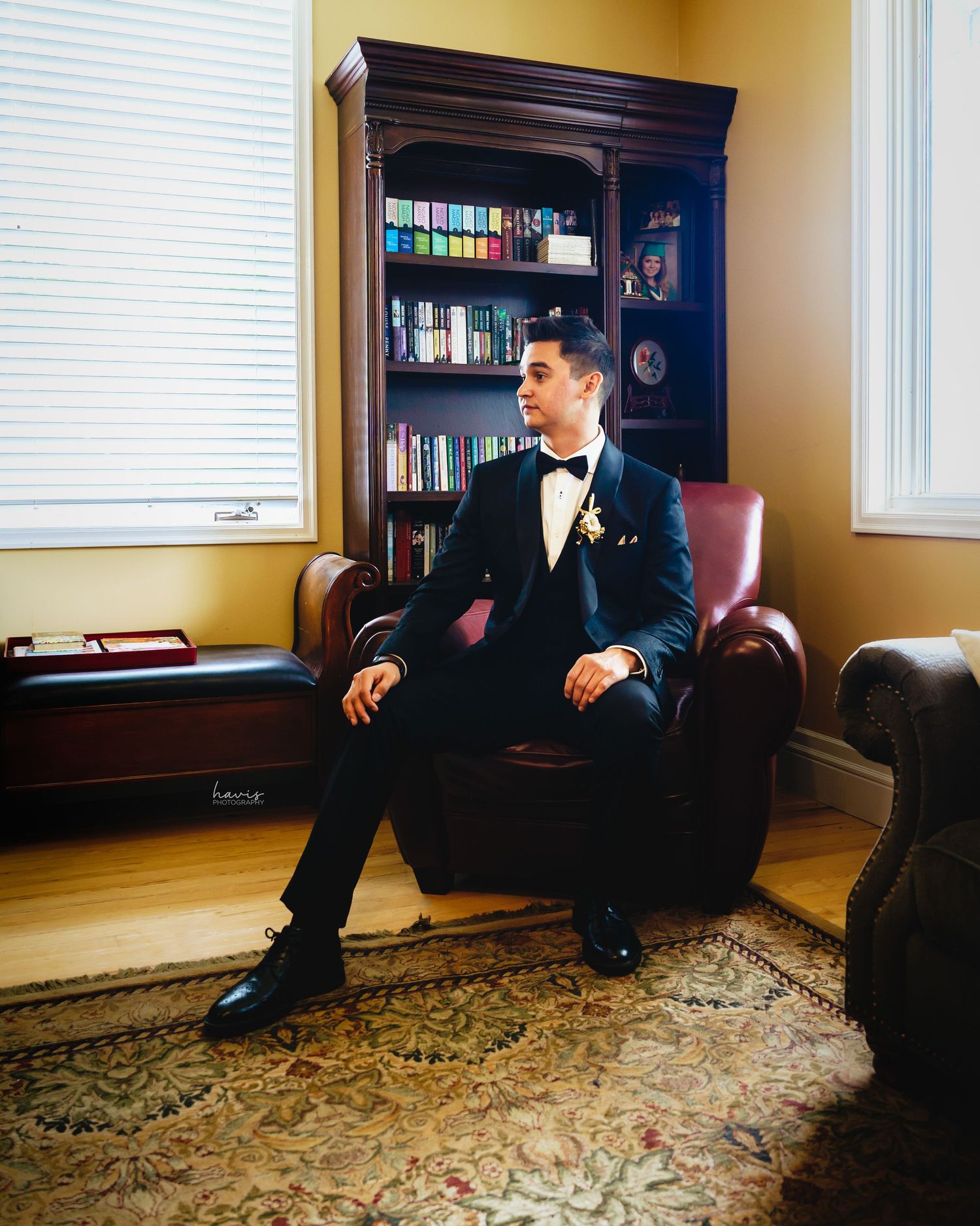 A groom in a black tuxedo posing for a photograph in a room on his wedding day